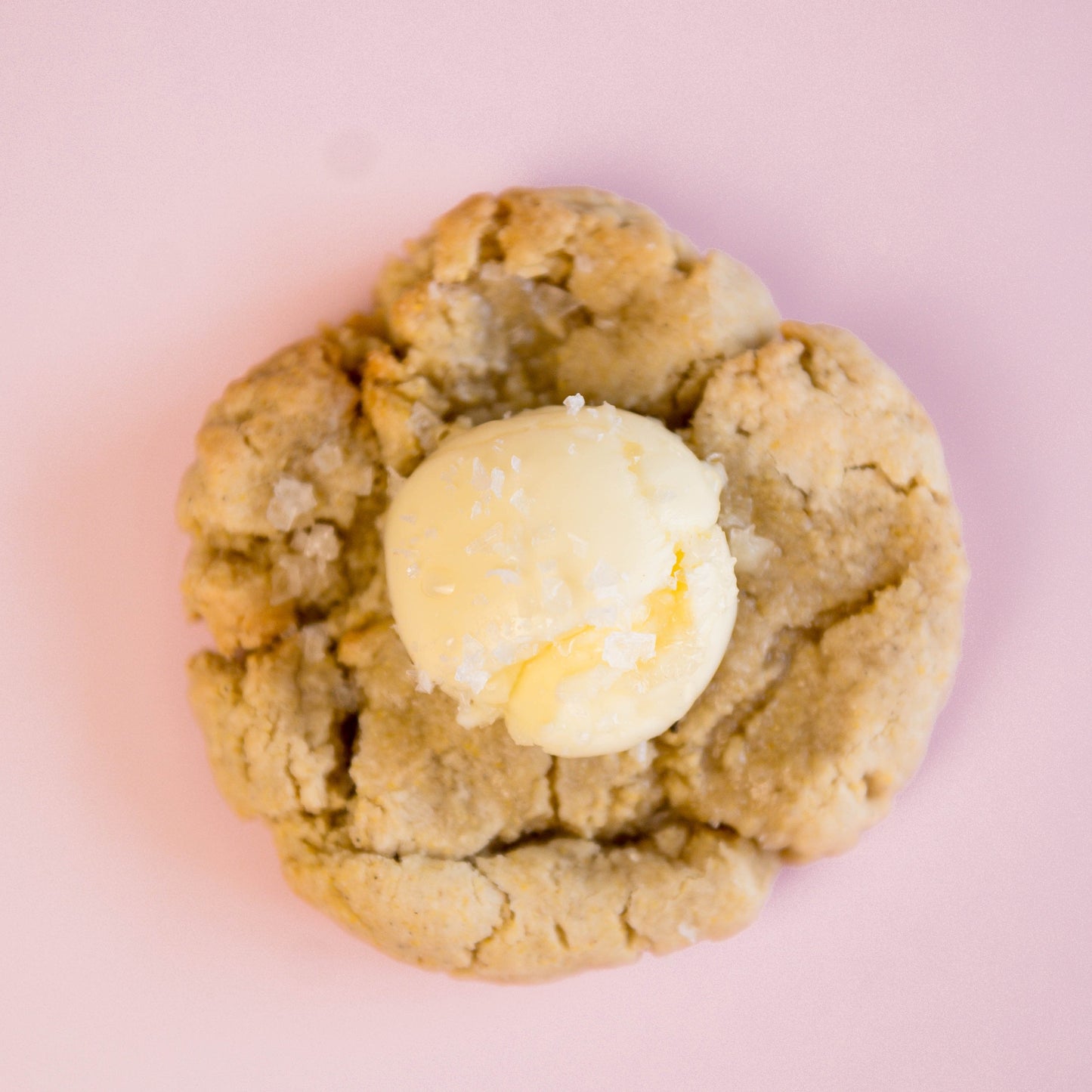 A single Salted Honey Cornbread - Gluten Free cookie from The Common Cookie, topped with vanilla ice cream, photographed on a light pink background.