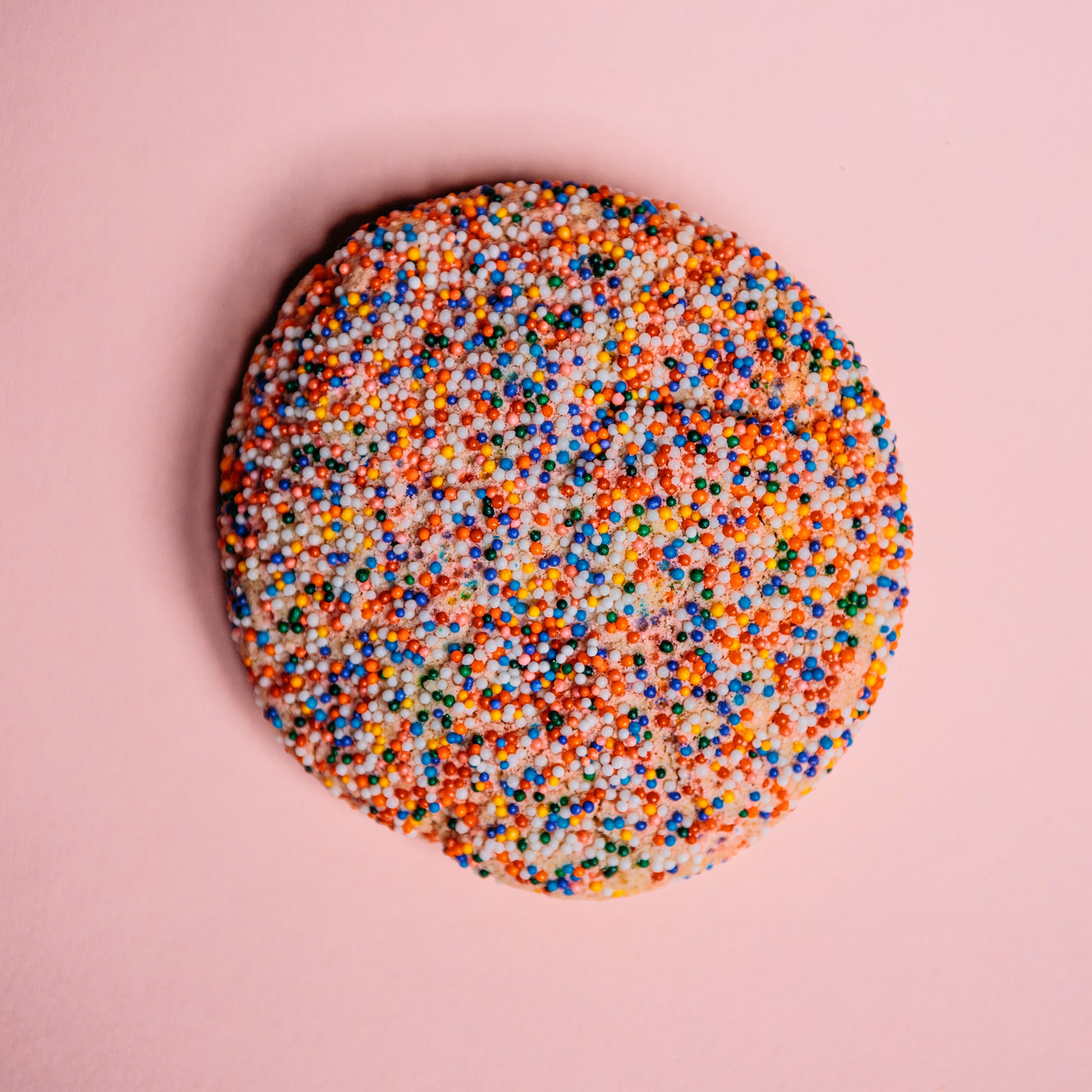 The Common Cookie's Almond Frangipane- Gluten Free features a buttery almond-scented dough adorned with colorful sprinkles on a pink background.