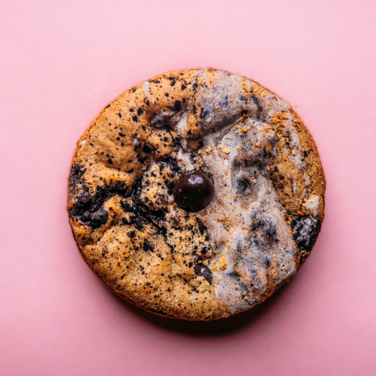 A round marbled Tiramisu- Gluten Free (Dozen) cookie by The Common Cookie with a single chocolate piece in the center, placed on a pink background.