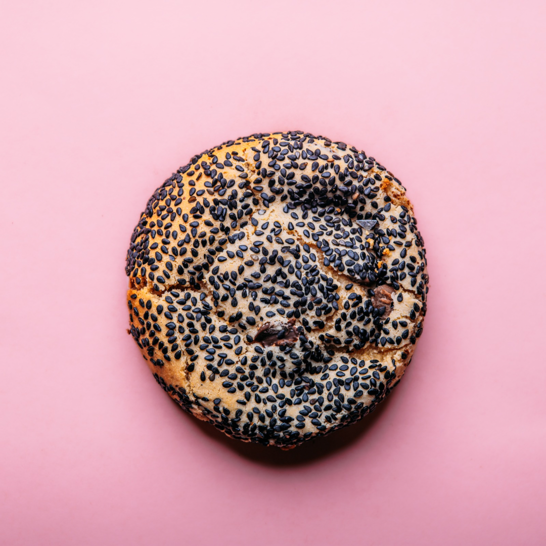 A dozen Tahini Chocolate Chip gluten-free cookies from The Common Cookie are arranged on a solid pink background.