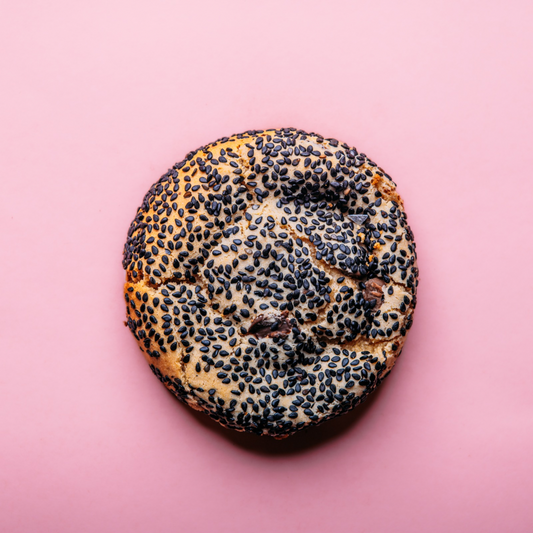 A dozen Tahini Chocolate Chip gluten-free cookies from The Common Cookie are arranged on a solid pink background.